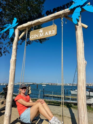 Beach Bar im Ostseeresort Olpenitz Frau auf einer Schaukel der Beach Bar mit Blick auf Hafenbecken und Ostseeresort Olpenitz.